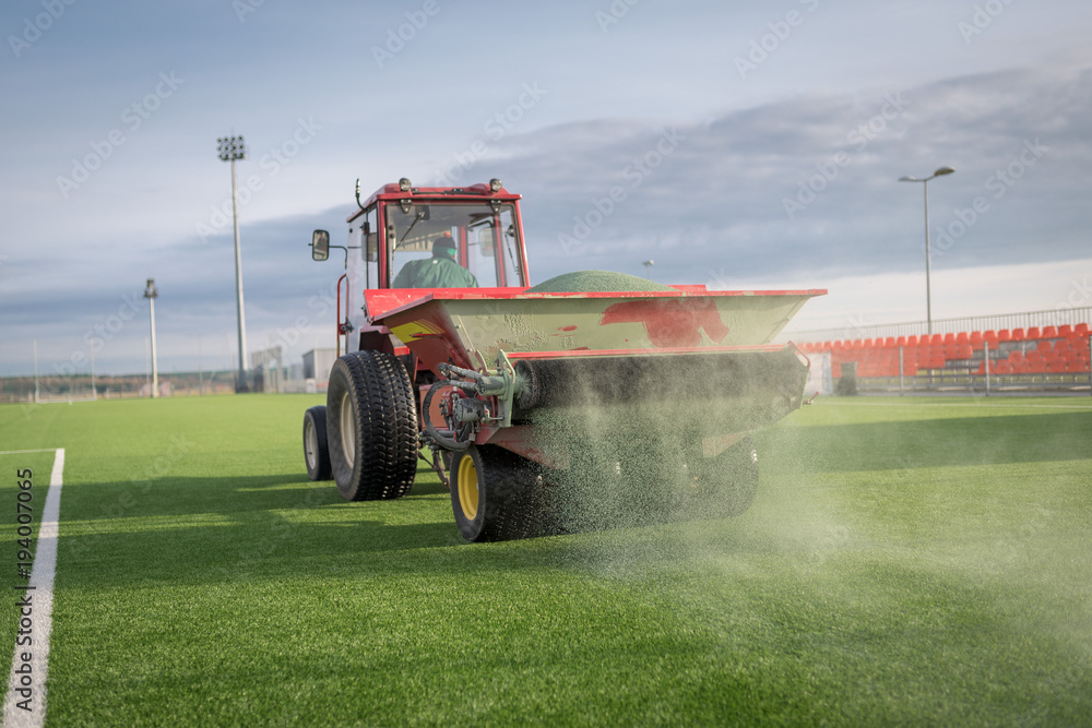 Naklejka premium Pouring infill granules in to a football pitch with artificial grass.