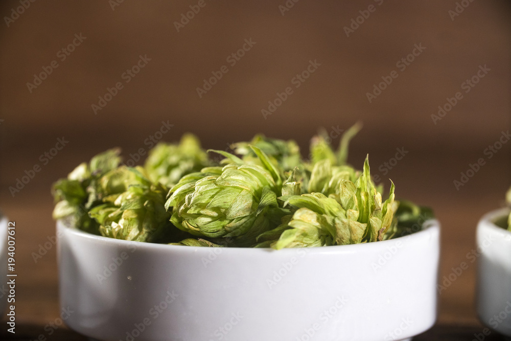 Beer brewing ingredients Hop cones in white bowl on wooden background. Beer brewery concept. Beer brewing ingredients Hop cones in white bowl on wooden background. Beer brewery concept.