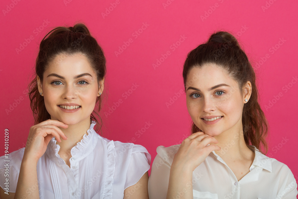 two beautiful young sisters twin girls with a smile on a pink background two beautiful young sisters twin girls with a smile on a pink background