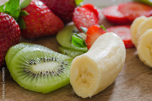 peeled bananas, sliced kiwi and sliced strawberries on a wooden floor