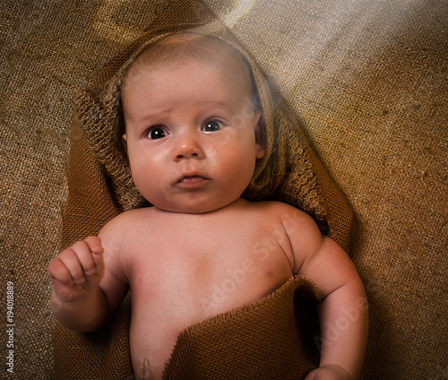 Valokuva Child in the image of an angel with a ray of light, wrapped in burlap