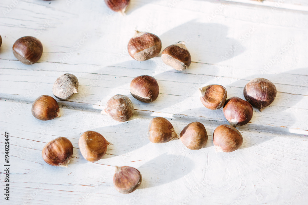 Obraz premium Fresh raw chestnuts on white wooden surface.