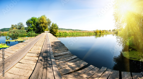 Wooden bridge over river with green trees under bright sun
