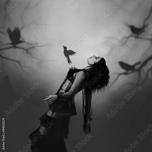 Canvastavla A girl in a black, vintage dress posing against the background of a gloomy forest, which is created by the projector