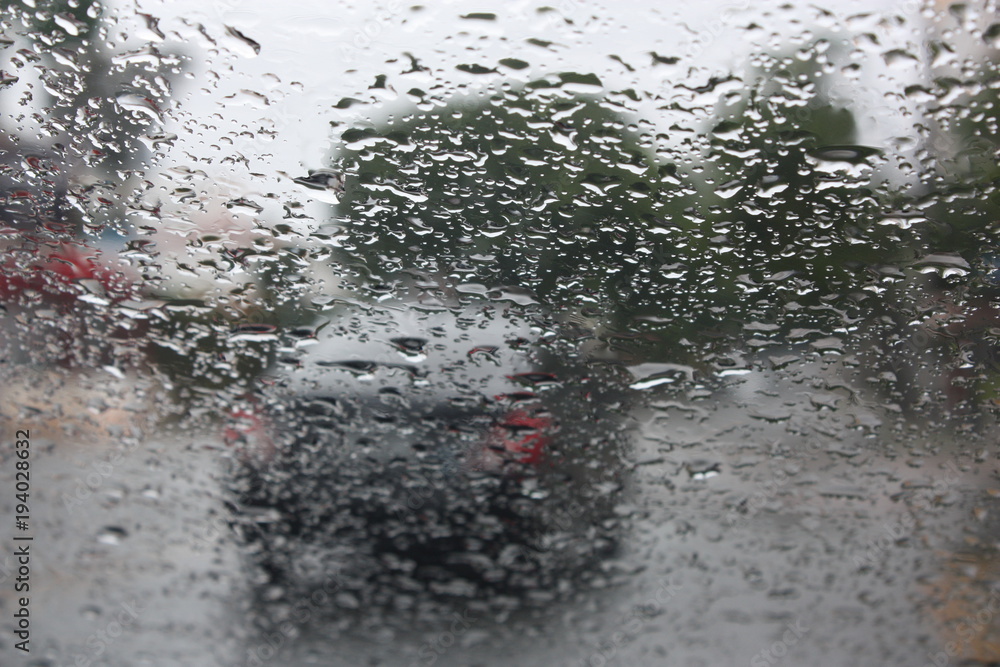 Raindrops on a glass window with blurry trees, road and car Raindrops on a glass window with blurry trees, road and car