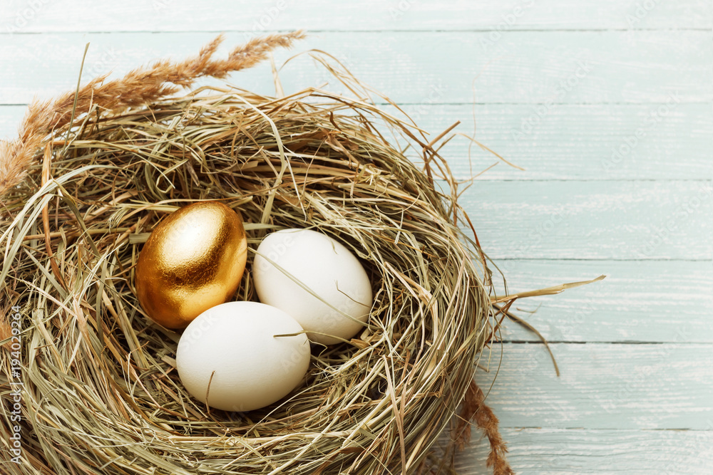 One gold and two ordinary eggs in the hay nest on light wooden bacground One gold and two ordinary eggs in the hay nest on light wooden bacground