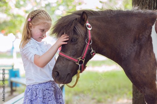 Little kid girl holding cuddling her pony horse isolated outdoors outside green park background