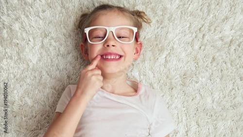 Beautiful little girl in glasses laughing and pointing at her toothy smile.