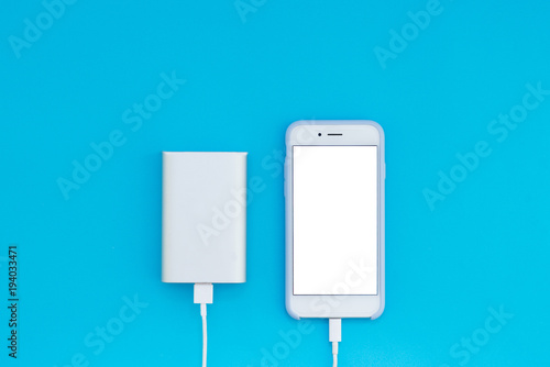 White smartphone and charger power bank on a blue background. Top view of the place for the text.