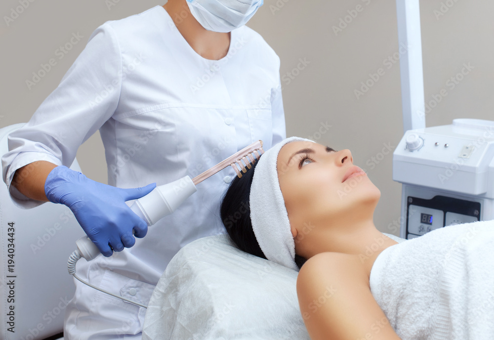 Obraz premium The doctor-cosmetologist makes the procedure Microcurrent therapy On the hair of a beautiful, young woman in a beauty salon.Cosmetology and professional skin care.