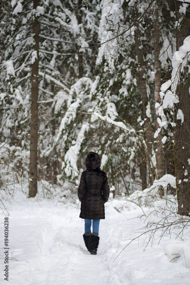 Back view on walking woman in winter snowy forest