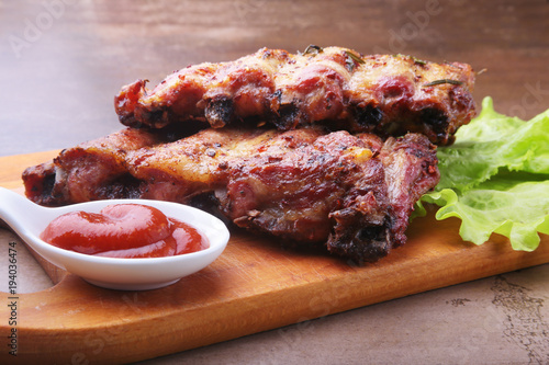 grilled barbecued ribs with lettuce leaves, hot chili pepper and sauce on wooden cutting board.