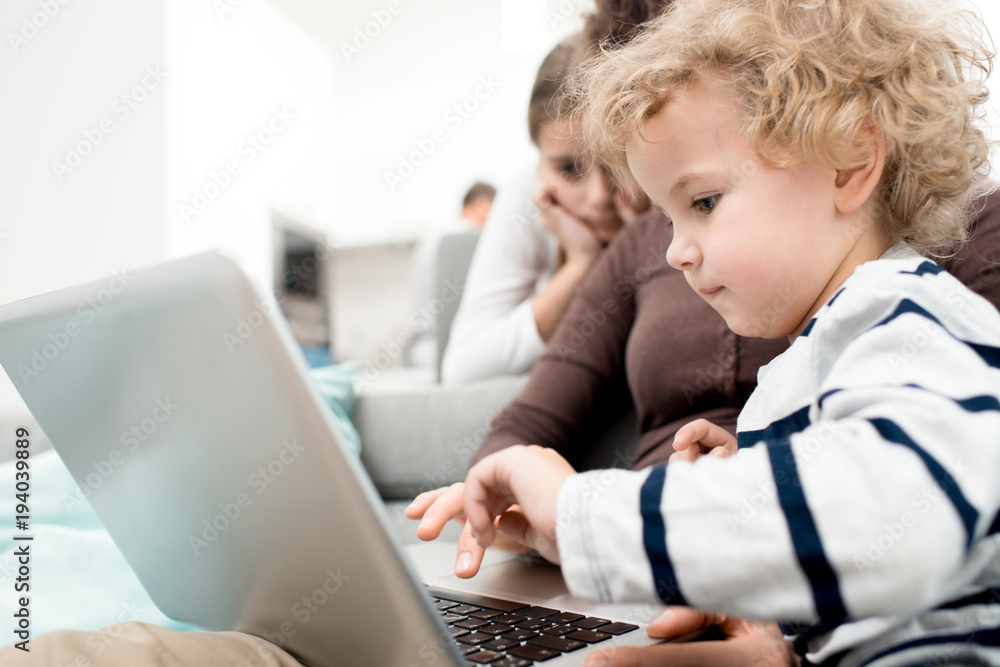 Side view portrait of cute blond toddler using laptop while watching cartoons with mom, copy space Side view portrait of cute blond toddler using laptop while watching cartoons with mom, copy space