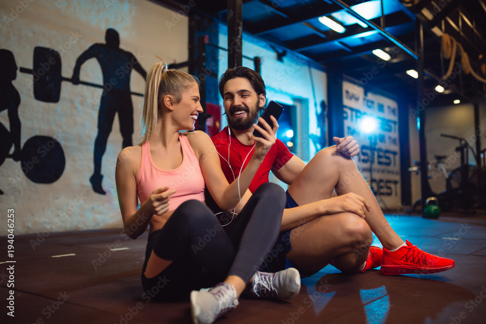 Obraz premium Fit couple in modern crossfit gym with smartphone listening to the music.