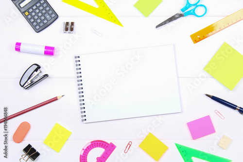 A blank notebook page surrounded by stationery on a white wooden table. Copy the space.