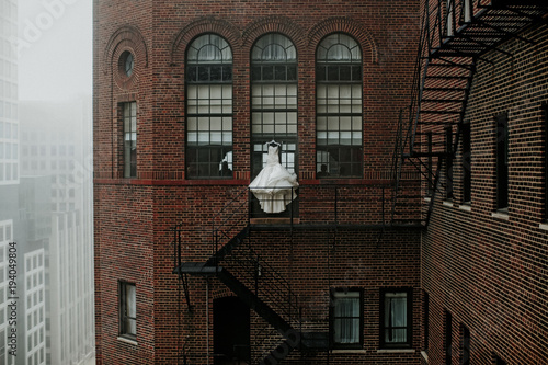 Wedding gown hanging by fire escape of building in city photo