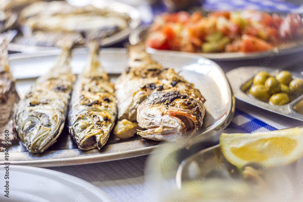 Barbecued sea bass, golden, horse mackerel accompanied with tomato salad, olives and white wine
