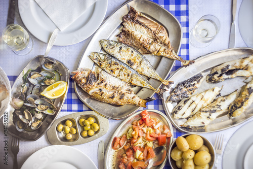 Barbecued sea bass, golden, horse mackerel accompanied with tomato salad, clams, bread and white wine