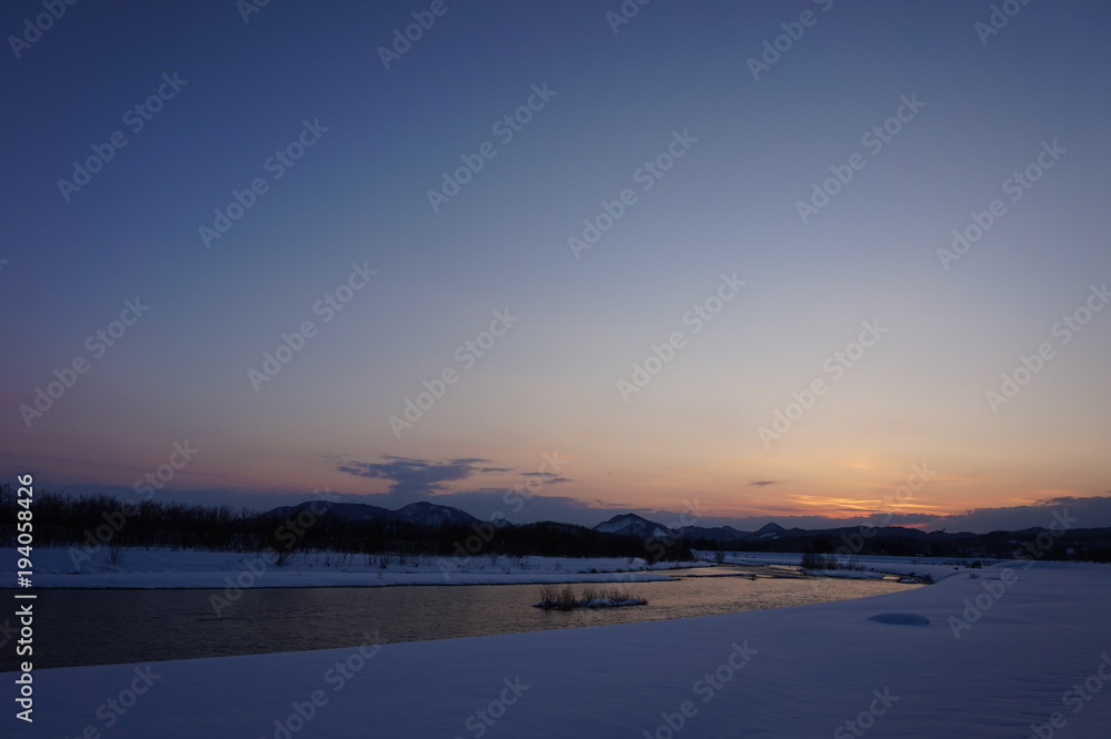 冬の夕暮れ　川　日没　雪景色　太陽