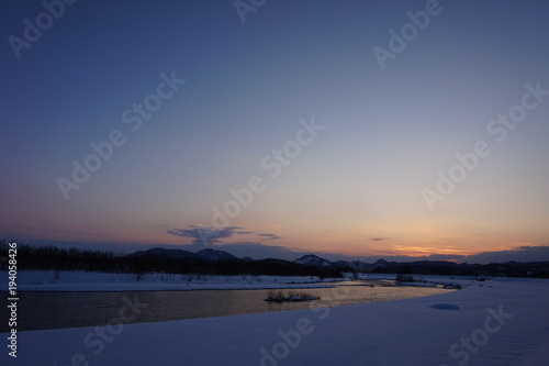 冬の夕暮れ　川　日没　雪景色　太陽 © amosfal