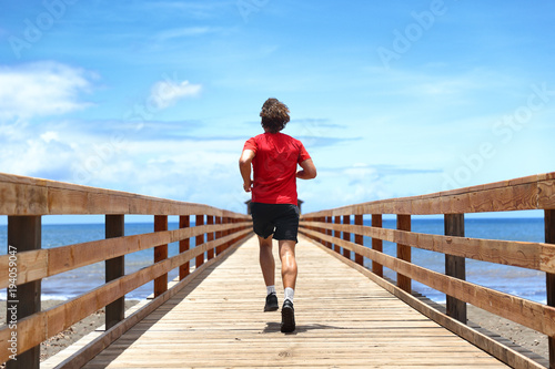 Fototapeta Naklejka Na Ścianę i Meble -  Running runner sport man jogging on beach boardwalk living active lifestyle. Workout outside person with fit body training for weight loss success, man taking step towards life happiness.