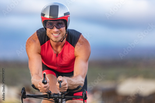 Triathlon biking man cyclist portrait riding bike. Male triathlete cycling on triathlon bike. Fit man professional athlete on triathlon bicycle wearing time trial helmet for ironman race.