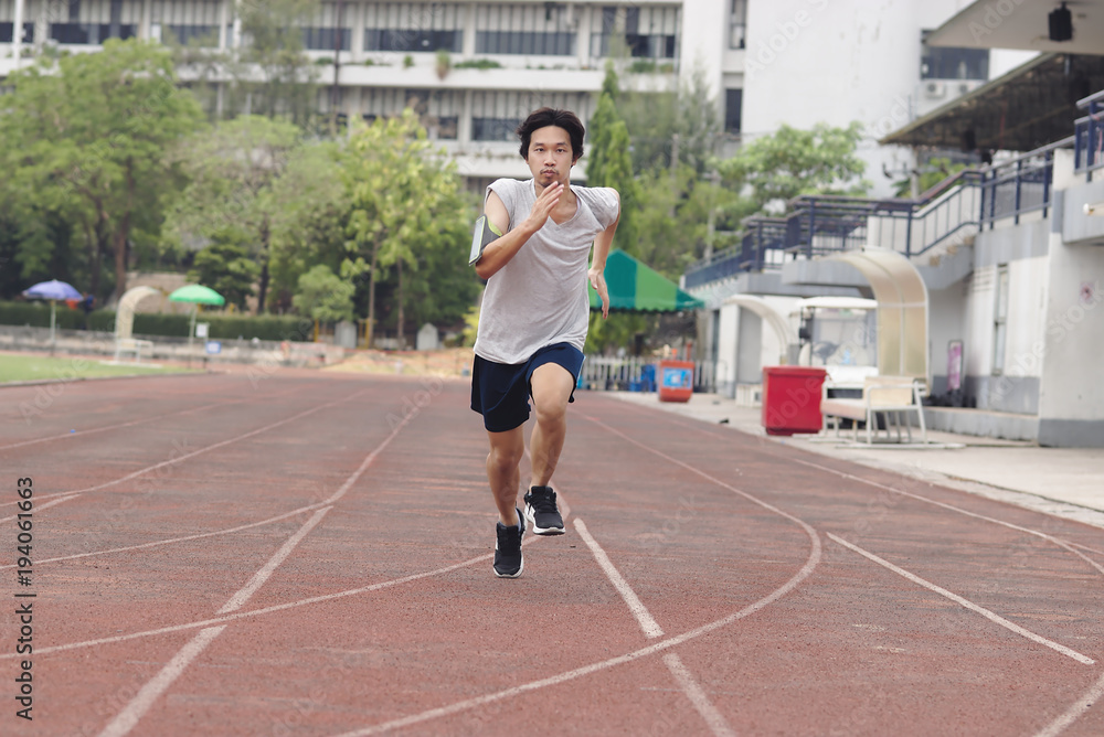 Handsome athlete Asian man running on racetrack in stadium with copy space background. Healthy active lifestyle concept.