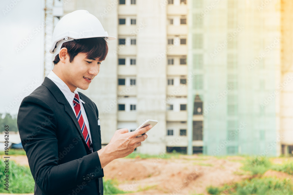 Fototapeta premium Asian engineer holding smartphone work concept teamwork of building construction. Project contractor reviewing plan work in construction site.
