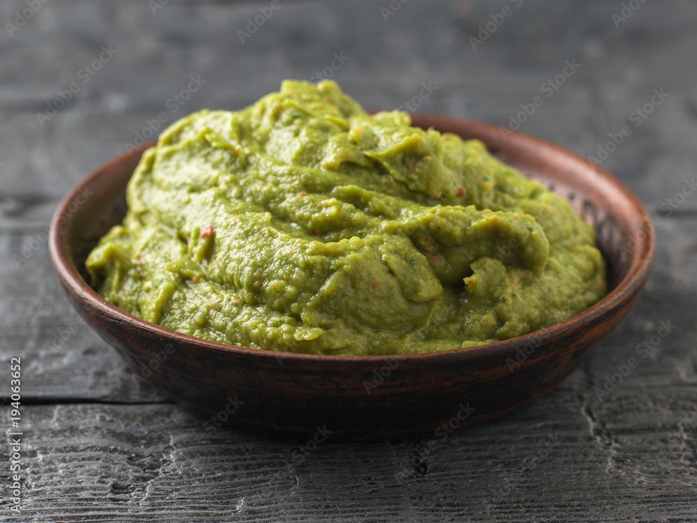 Freshly made guacamole in a clay bowl on a dark rustic table. Raw food. Freshly made guacamole in a clay bowl on a dark rustic table. Raw food.