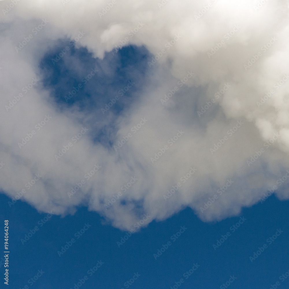 A hole in the form of a heart in white smoke against a blue sky. Background for design. Copy space.