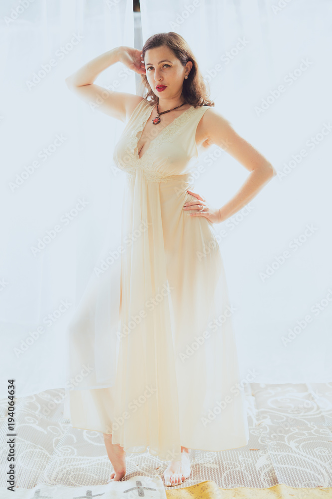 Young woman in retro pin up style and white dress poses against a white curtain backdrop