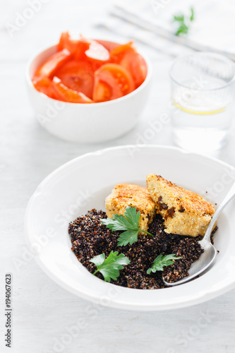 Vegetarian dinner table. Plate with black quinoa and oatmeal cutlets with prunes on white wooden table with tomato salad and water with lemon, top view