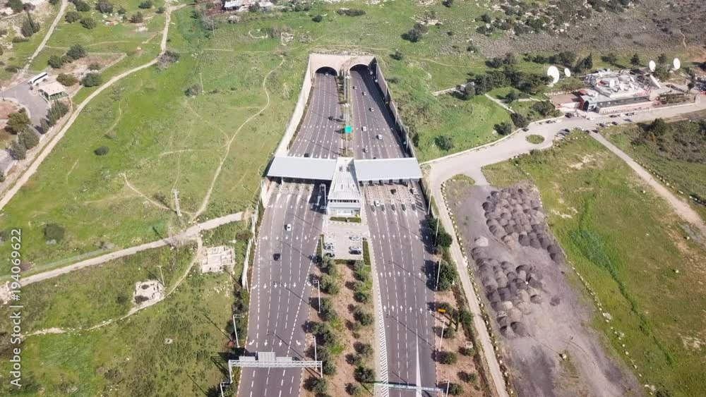 Highway traffic entering and exiting a Toll collection stop leading to a double tunnel surrounded by green landscape - Aerial footage Highway traffic entering and exiting a Toll collection stop leading to a double tunnel surrounded by green landscape - Aerial footage