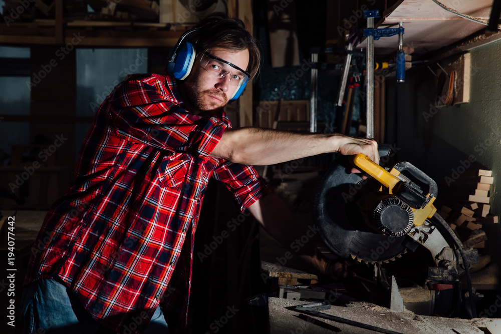 brunette man profession carpenter builder saws with a circular saw a wooden board.
