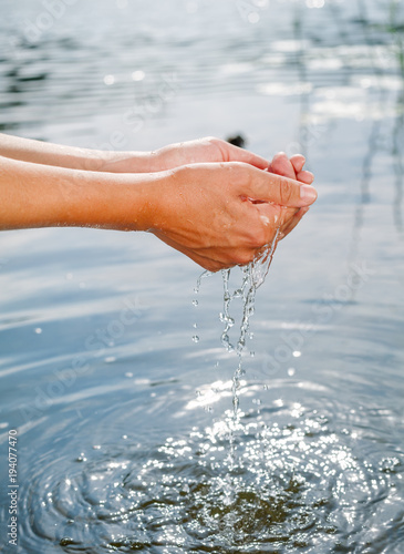 Person taking raw unfiltered water from a lake by hands