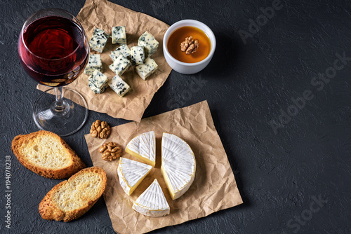 Camembert cheese, blue cheese, toasts, honey, walnuts and glass of wine on a dark background. Flat Lay.