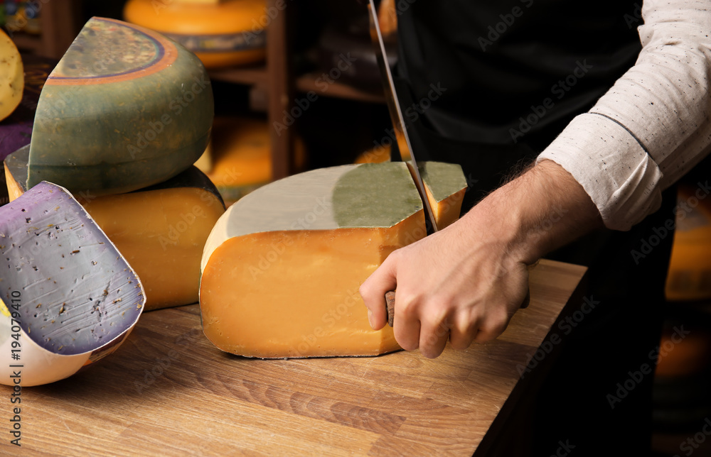 Fotografie Young worker cutting cheese in shop