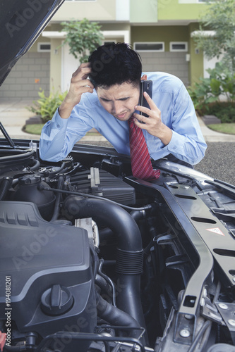 Stressed businessman checking on the engine of the damaged car © Creativa Images