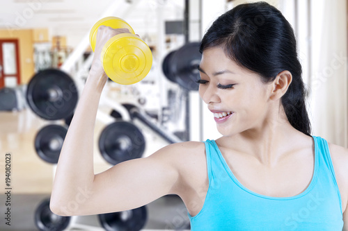 Beautiful asian woman smiling to camera while lifting dumbbell