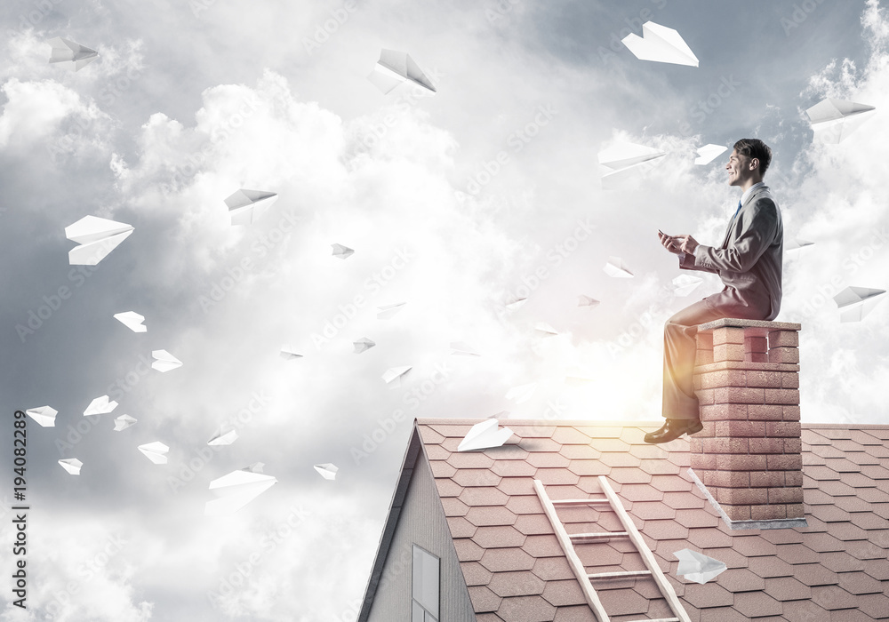 Man on brick roof reading book and paper planes flying in air Man on brick roof reading book and paper planes flying in air