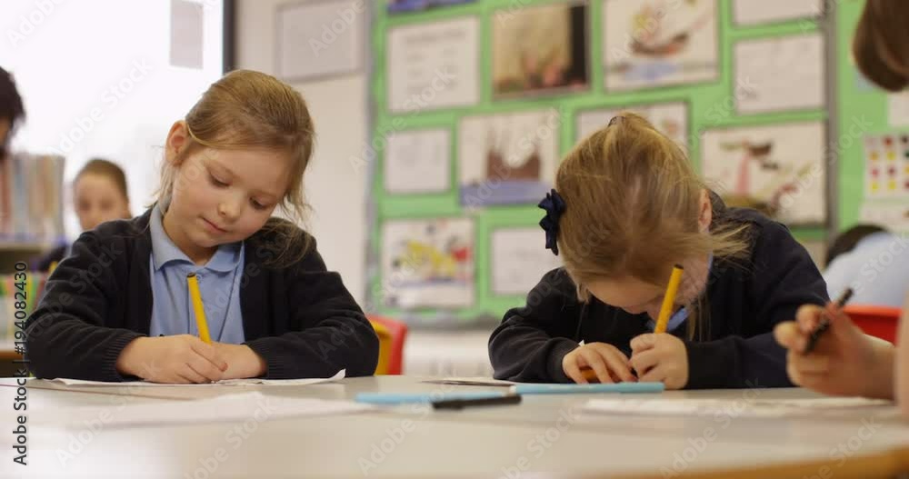 4k, Two cute little girls sitting in class with her teacher and classmates blurred in the background. Slow motion. 4k, Two cute little girls sitting in class with her teacher and classmates blurred in the background. Slow motion.