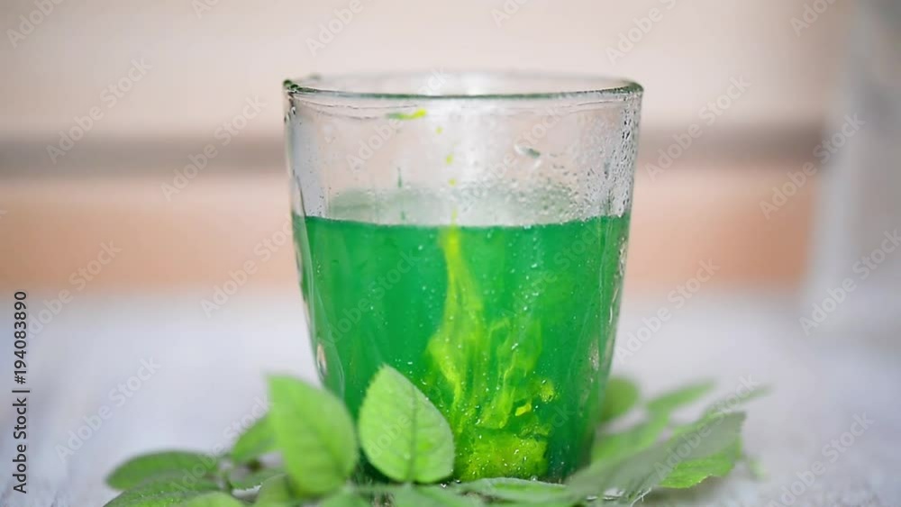 In water in a transparent glass with a brush to mix green paint. Symbol of freshness and purity. Added a drop of yellow paint. Color mixing In water in a transparent glass with a brush to mix green paint. Symbol of freshness and purity. Added a drop of yellow paint. Color mixing