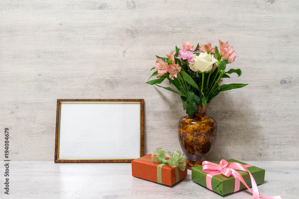 Colorful spring bouquet of rose, chrysanthemum and alstroemeria flowers in a vase with empty photoframe and gift boxes on wooden background Colorful spring bouquet of rose, chrysanthemum and alstroemeria flowers in a vase with empty photoframe and gift boxes on wooden background