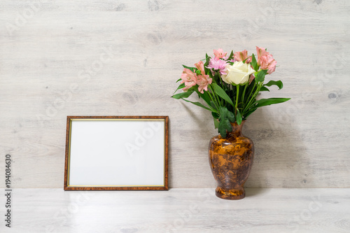 Fototapeta Naklejka Na Ścianę i Meble -  Colorful spring bouquet of rose, chrysanthemum and alstroemeria flowers in a vase with empty photoframe on wooden background