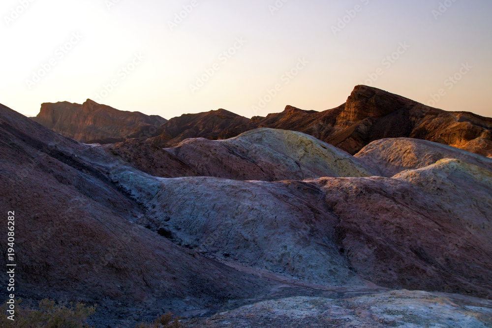 Fototapeta premium Setting Sun on the colorful eroded mountains ridges, ancient rock formations of the hottest place on earth, Death Valley National Park, Zabriskie Point peak, road trip the Amargosa Range, California
