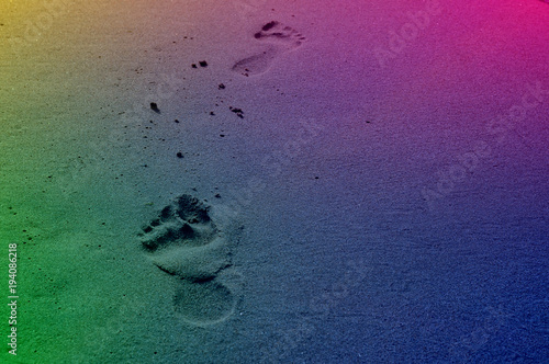 Ślady stóp w kolorach tęczy na plaży.