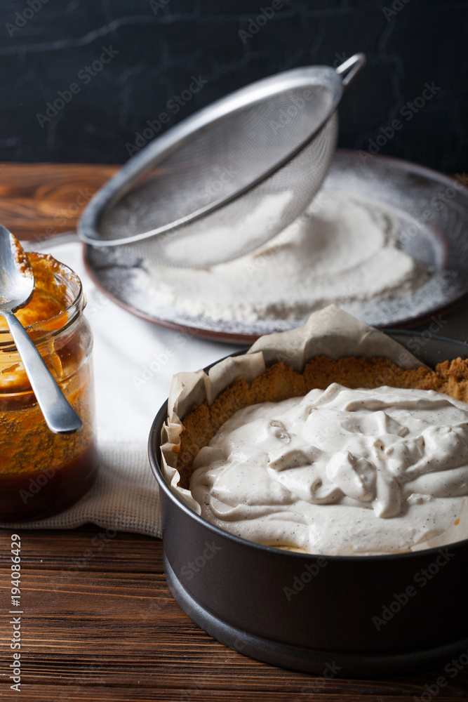 Fototapeta premium Banoffee pie with a jar of caramel and flour on the wooden background