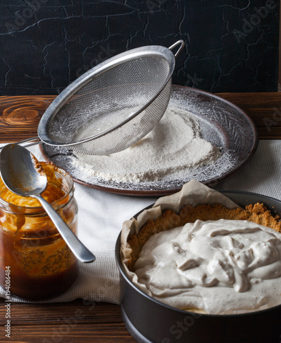 Moody Banoffee pie closeup with a jar of caramel and flour on a wooden background
