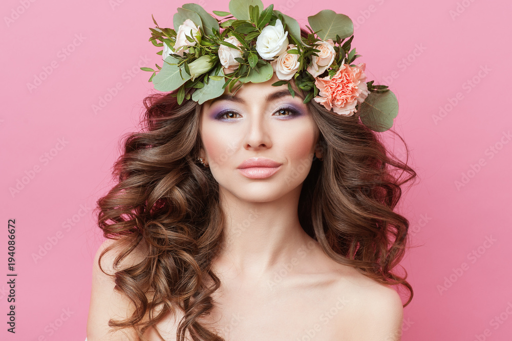 Portrait of beautiful young sexual sensual woman with perfect skin make up curly hair and flowers on head on pink background. Wreath of flowers Spring Summer Fashion Lifestyle People concepts.