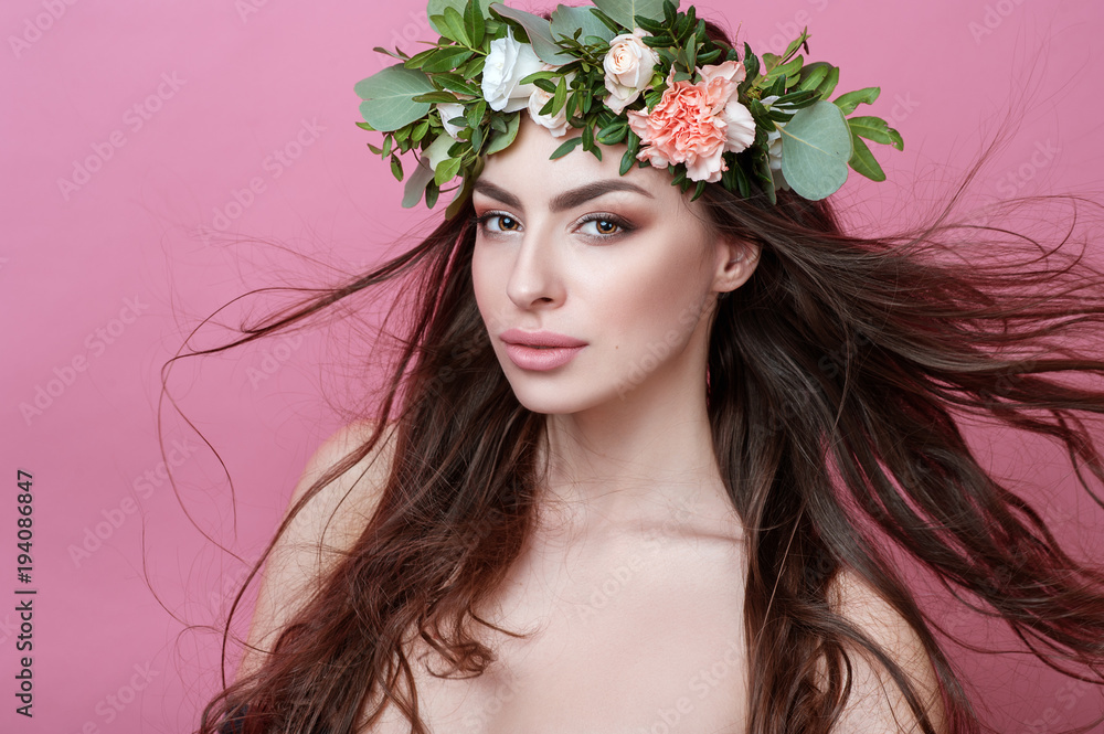 Portrait of beautiful young sexual sensual woman with perfect skin make up streaming hair and flowers on head on pink background. Wreath of flowers Spring Summer Fashion Lifestyle People concepts.